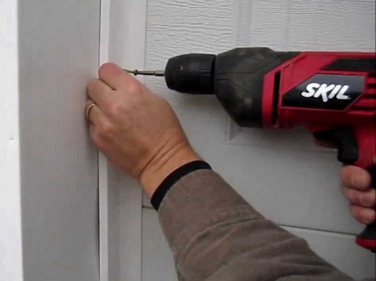 Homeowner using electric drill to install weatherstripping to residential garage door