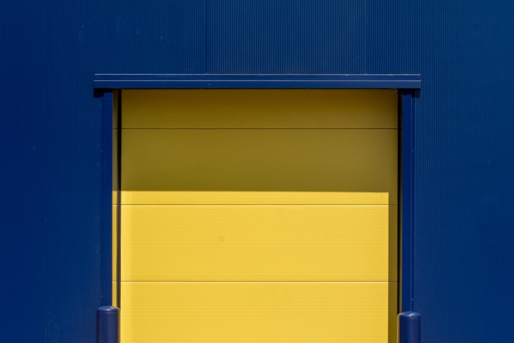 Bright yellow paneled single-car garage door with two rows of windows on dark commercial blue building