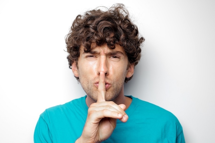 Man in blue shirt holding index finger to his lips