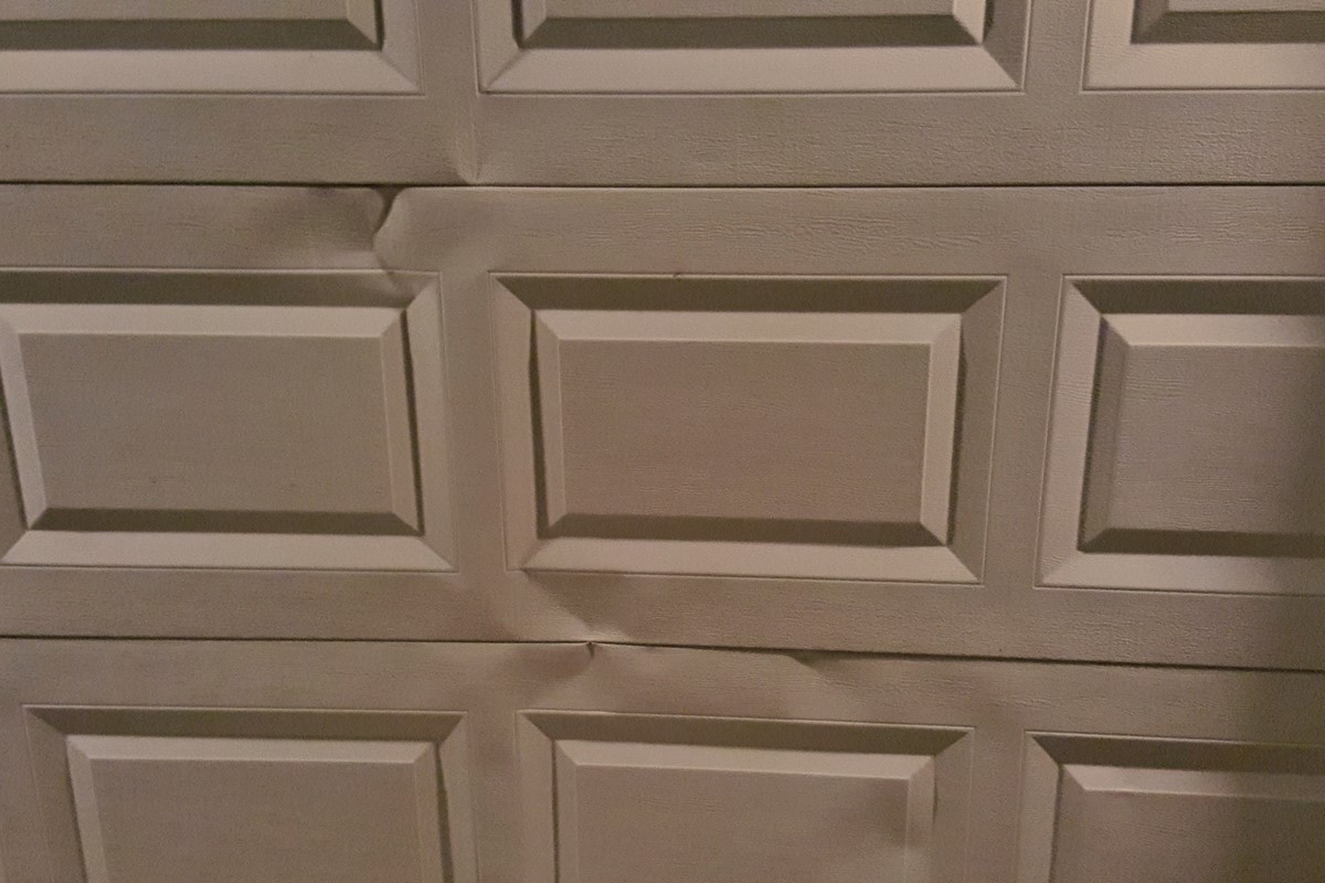 White paneled garage door with noticable indentation in steel surface