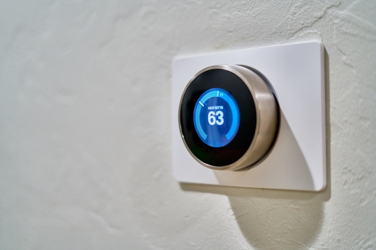 Smart thermos stat on white indoor wall displaying temperature of 63 degrees