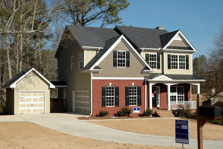 House with two-car garage and sold sign in yard beneath blowing treets on windy day