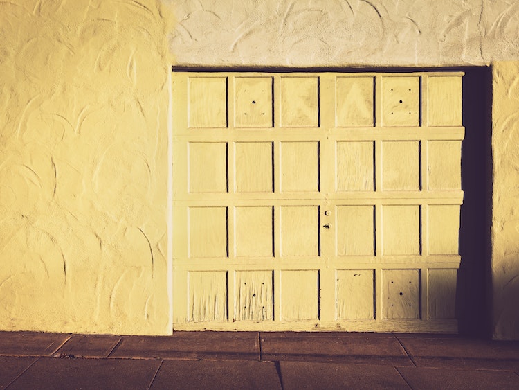 Yellow one-car garage with paneled garage door and chipping paint