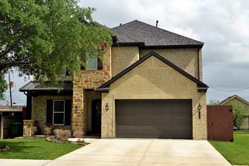 House with beige and stone exterior and dark brown two-car garage door on sunny summer day in Denver