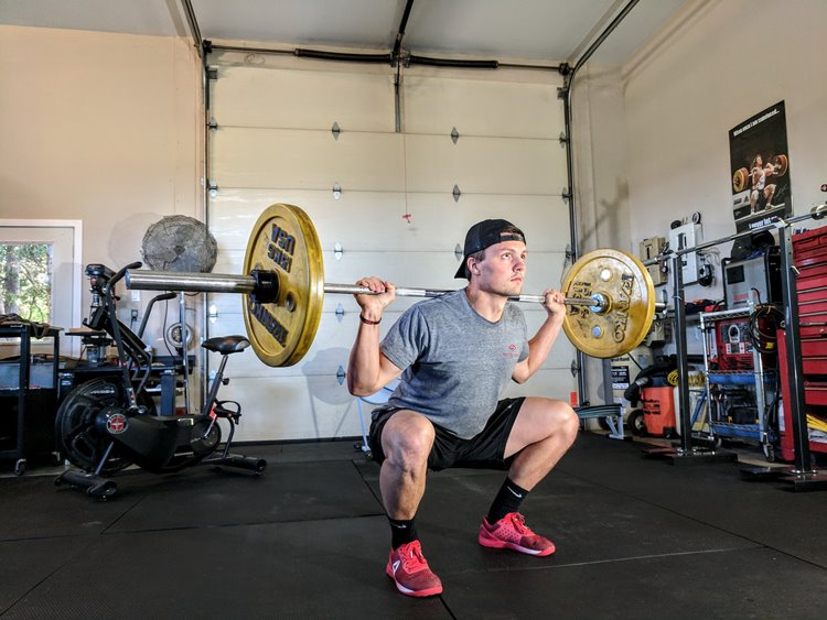 Man wearing gray t-shirt lifting weights in home gym beside garage door