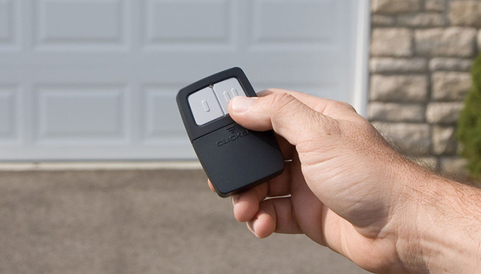 Hand pressing garage door opener remote button in driveway beside white paneled garage doors