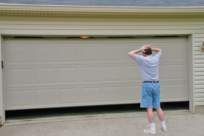 Confused homeowner standing by garage door with hands on his head