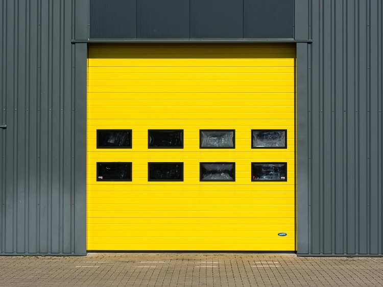 Bright yellow painted garage door with eight windows on dark teal industrial building