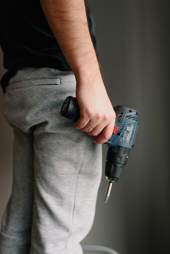 Ameteur repairman holding drill in everyday clothing before attempting DIY home repair