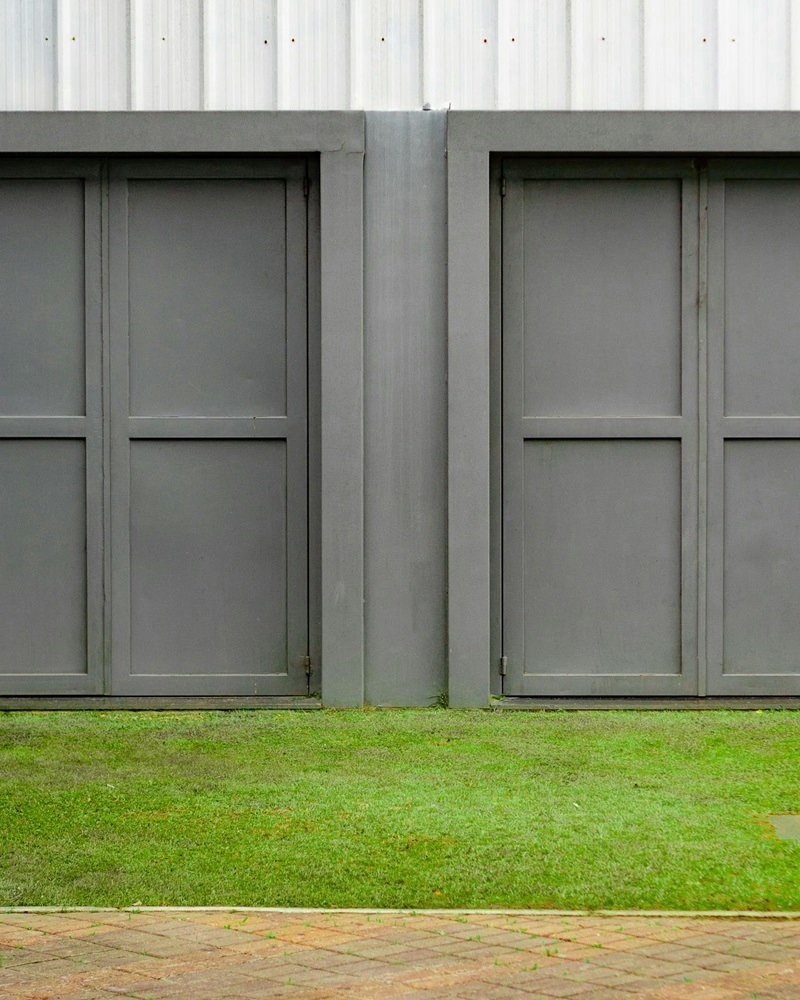 Two adjacent gray garage doors with damaged panels