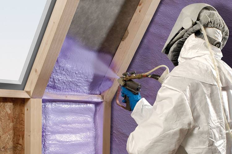 Technician in protective gear adding insulation to interior of home being built