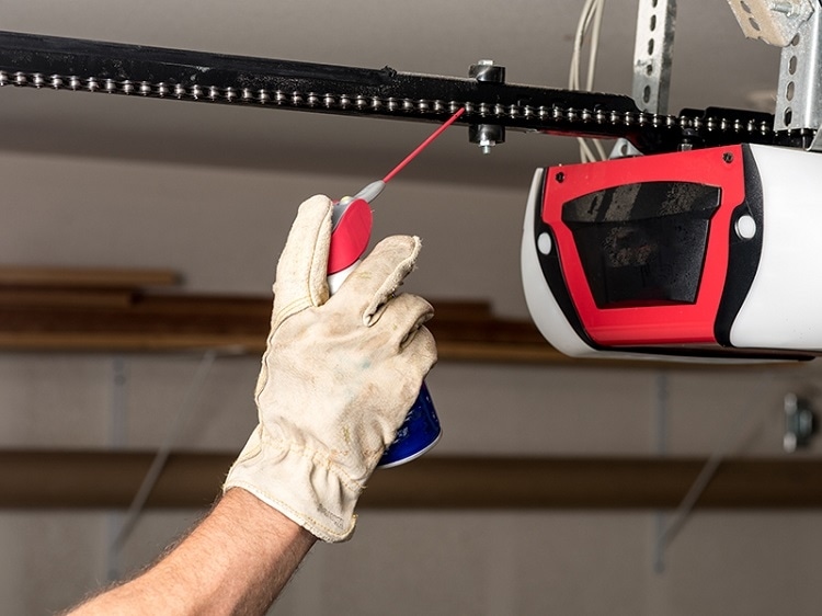 Gloved hand applying garage door lubricant to belt drive garage door opener