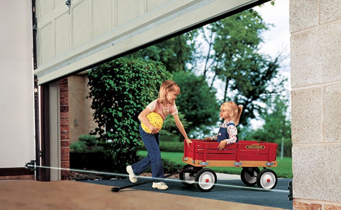 Smiling Girl Pulling Brother in Red Wagon Beneath Partially Open Garage Door into Open Space in Residential Garage